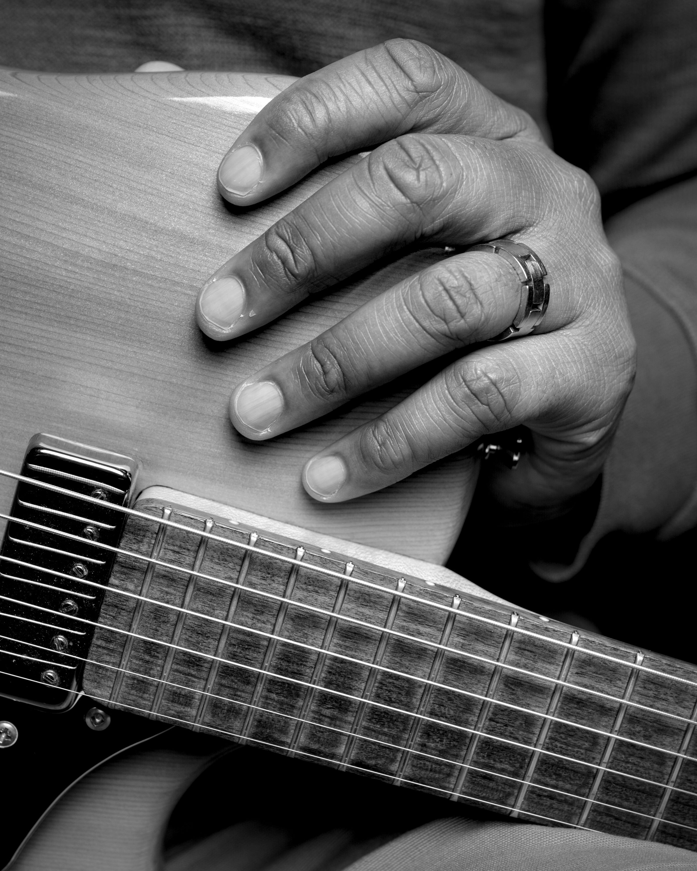Close view of a hand with a ring resting on the body of an electric guitar above the strings and fretboard.