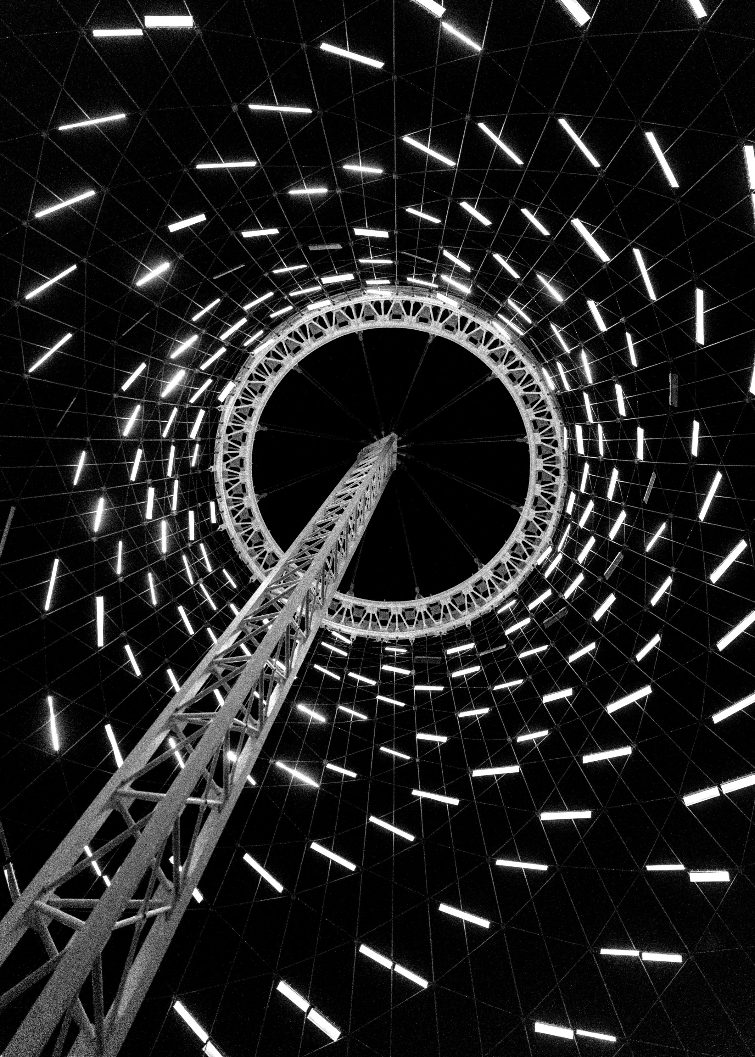 Upward view of a lattice tower inside a circular domed structure lined with rings of lights.