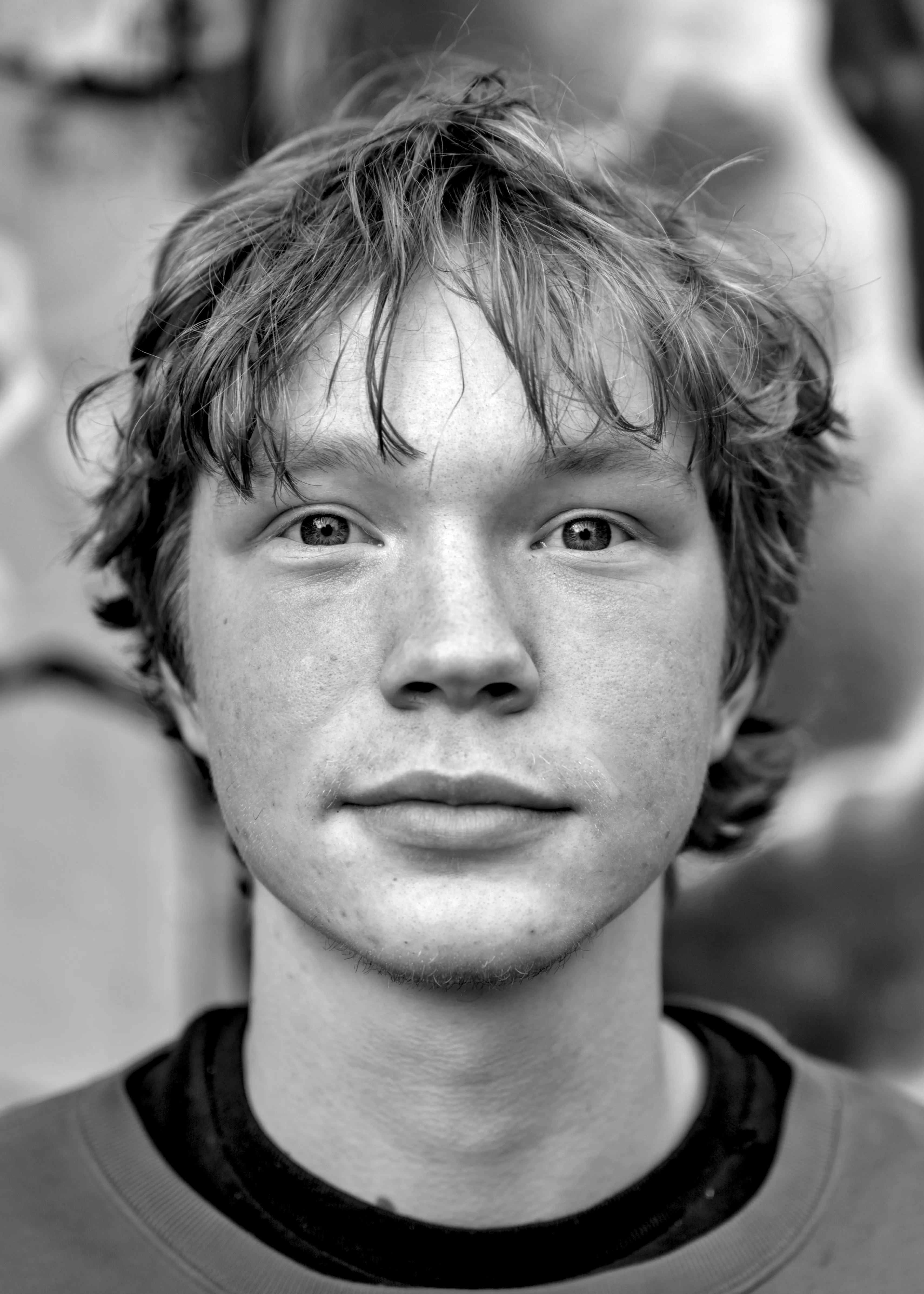 Close frontal portrait of a young man with tousled hair and a neutral expression, wearing a crew-neck sweatshirt.