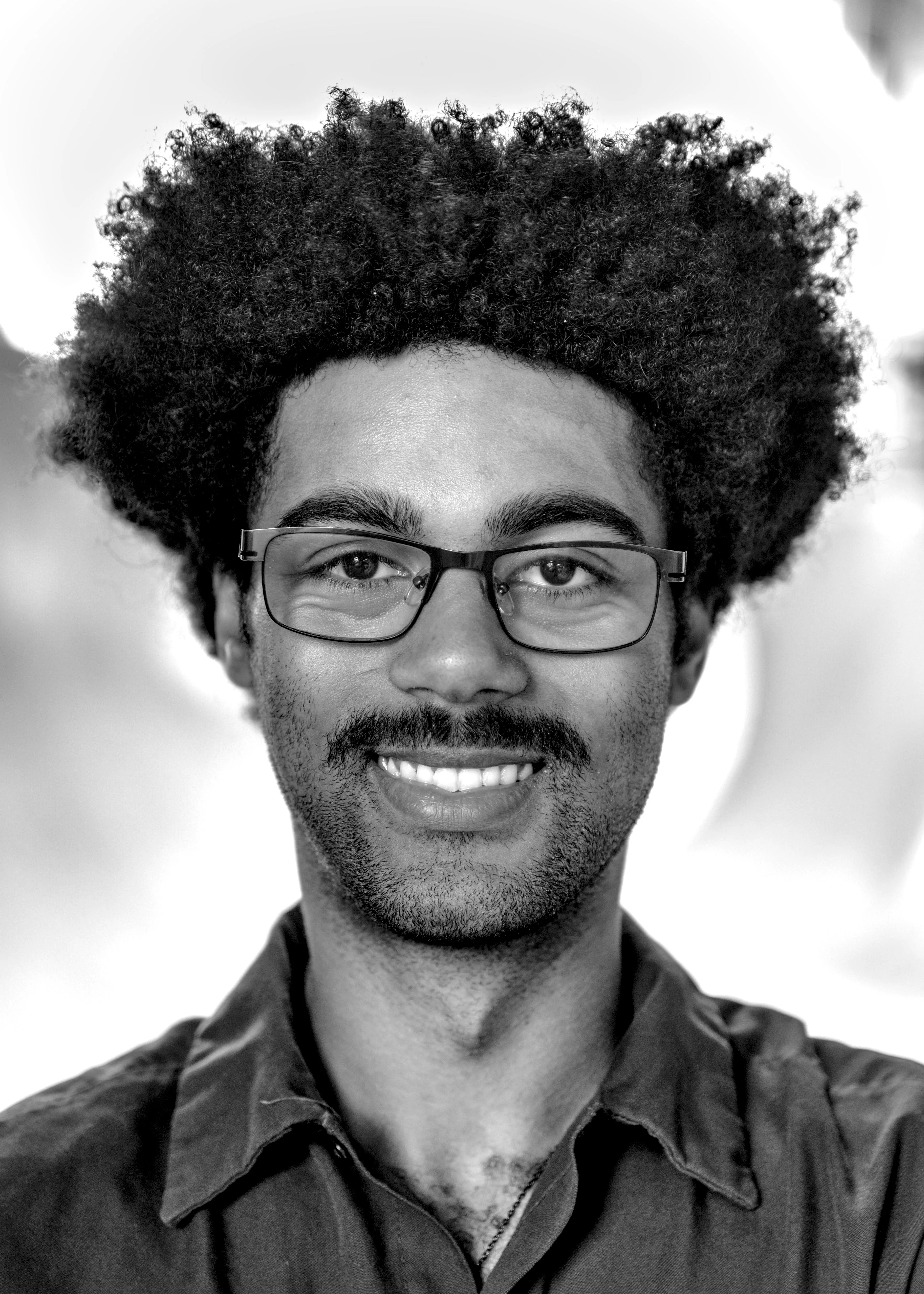 Portrait of a smiling man with a large afro, glasses and a mustache, wearing a collared shirt.